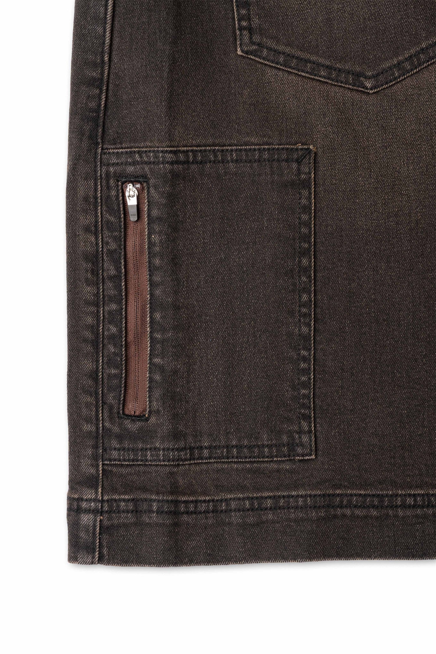 Close-up of a dark denim pocket with a zipper on a plain background