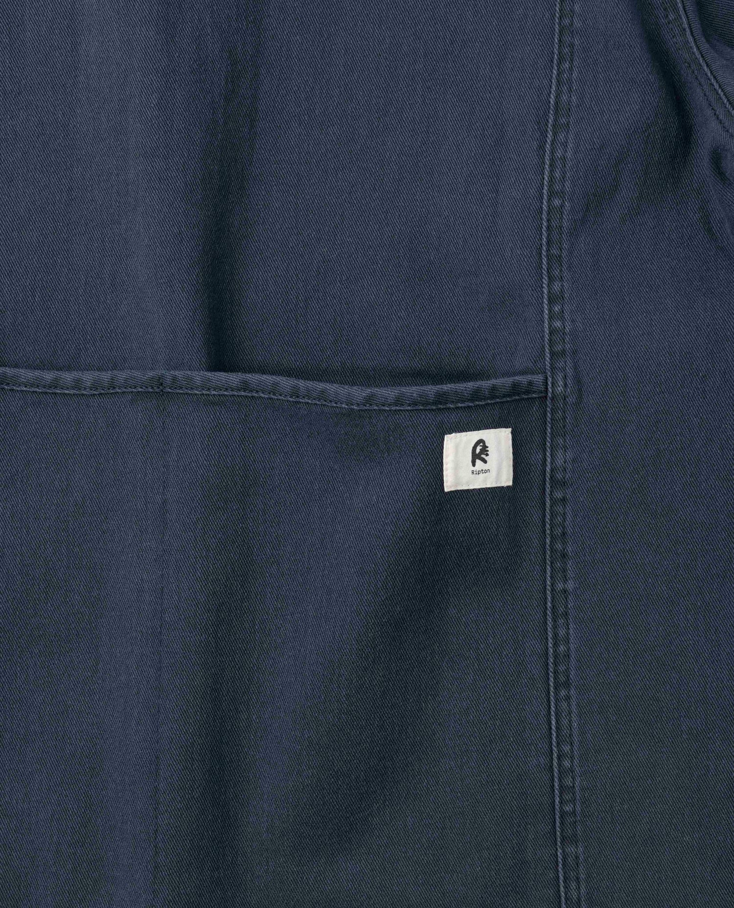 A close up photo of the texture of Ripton Sport Utility Pants in Navy. There is a small white Ripton branded tag on the right side of the pant.