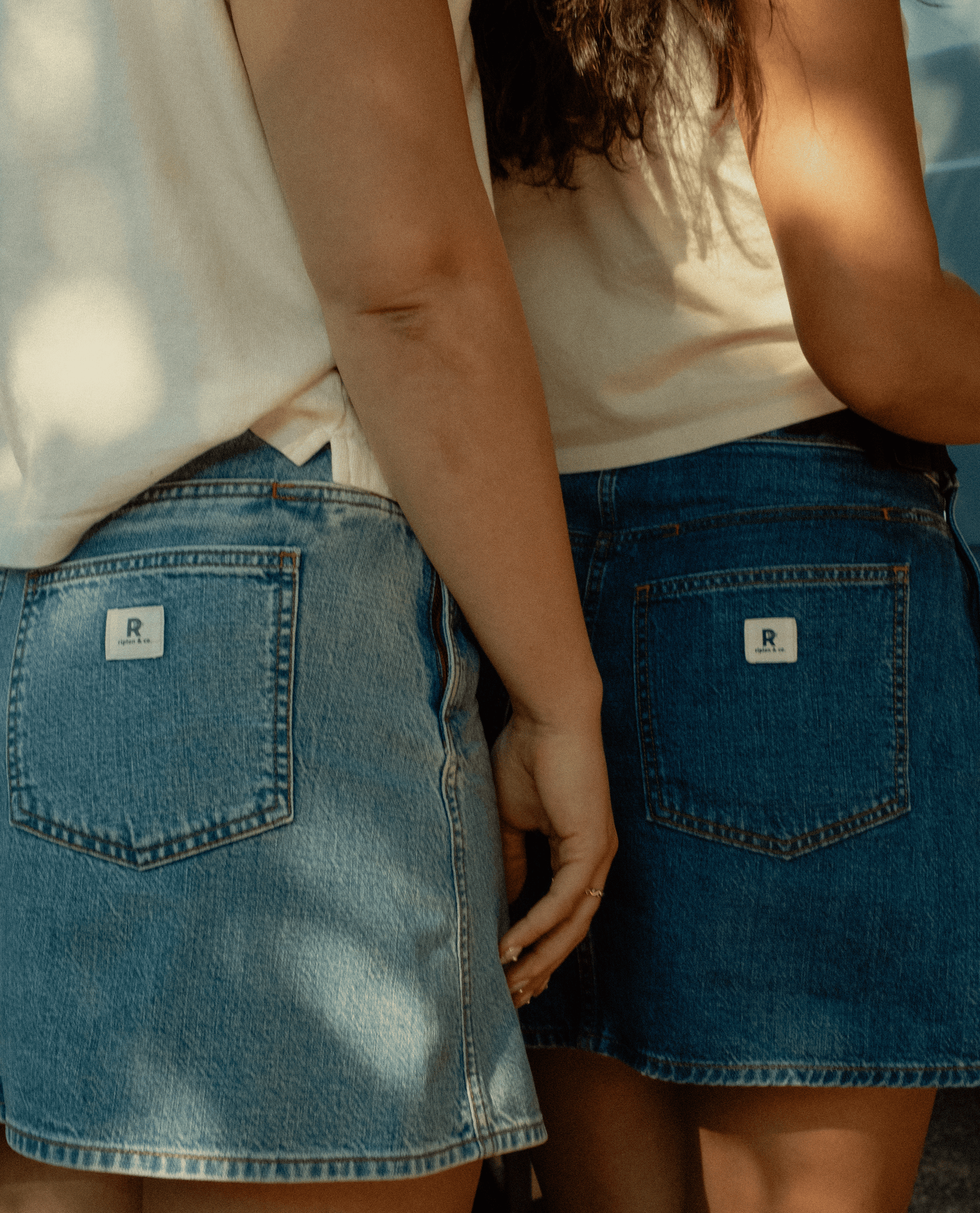Two girls wearing jean skirts and white shirts.