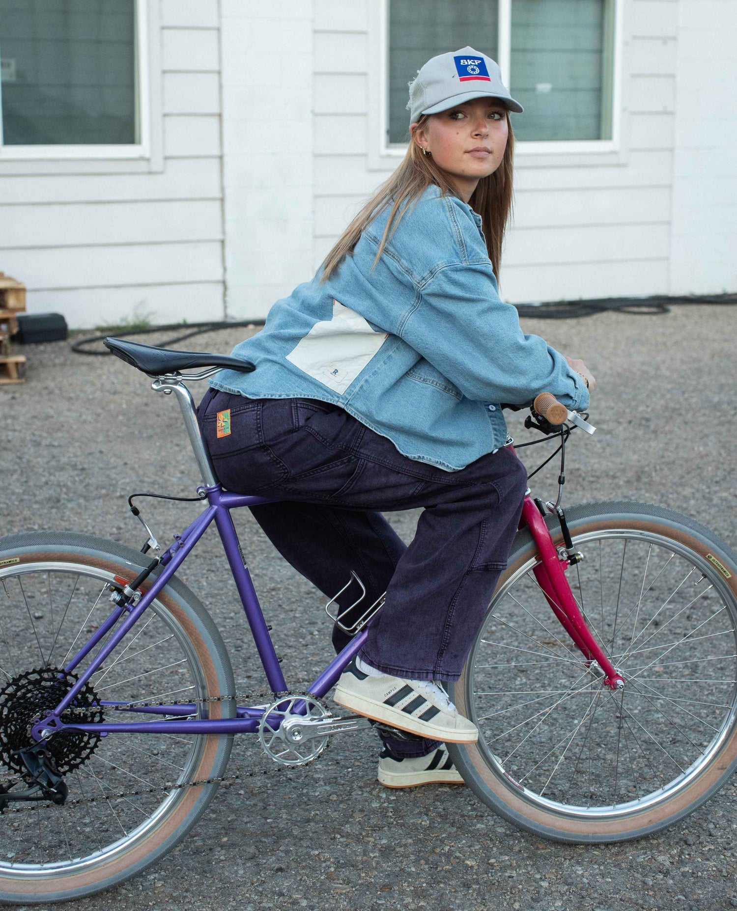 Person riding a bicycle wearing a denim jacket and cap with a logo.