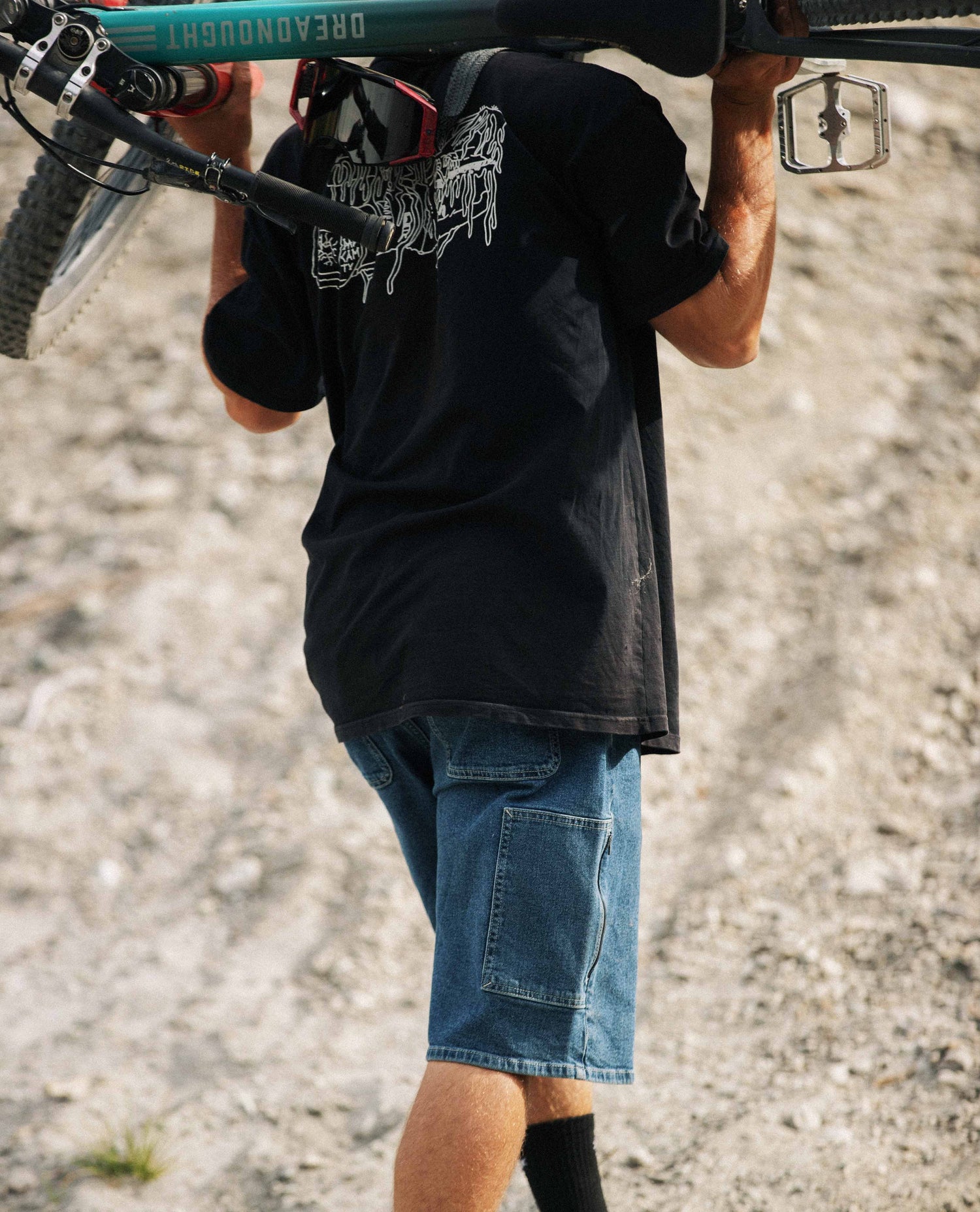 Person carrying a mountain bike over their shoulder on a gravel path