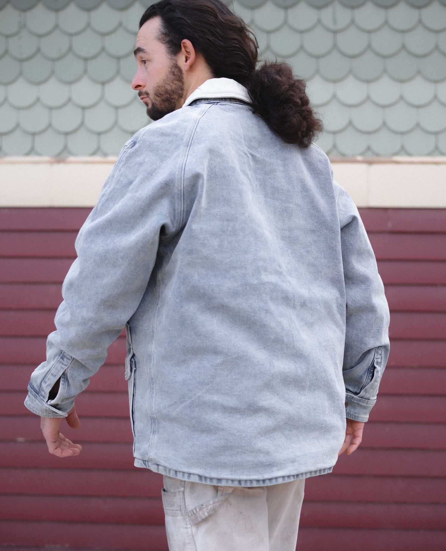 Person wearing a light gray jacket with a textured wall background