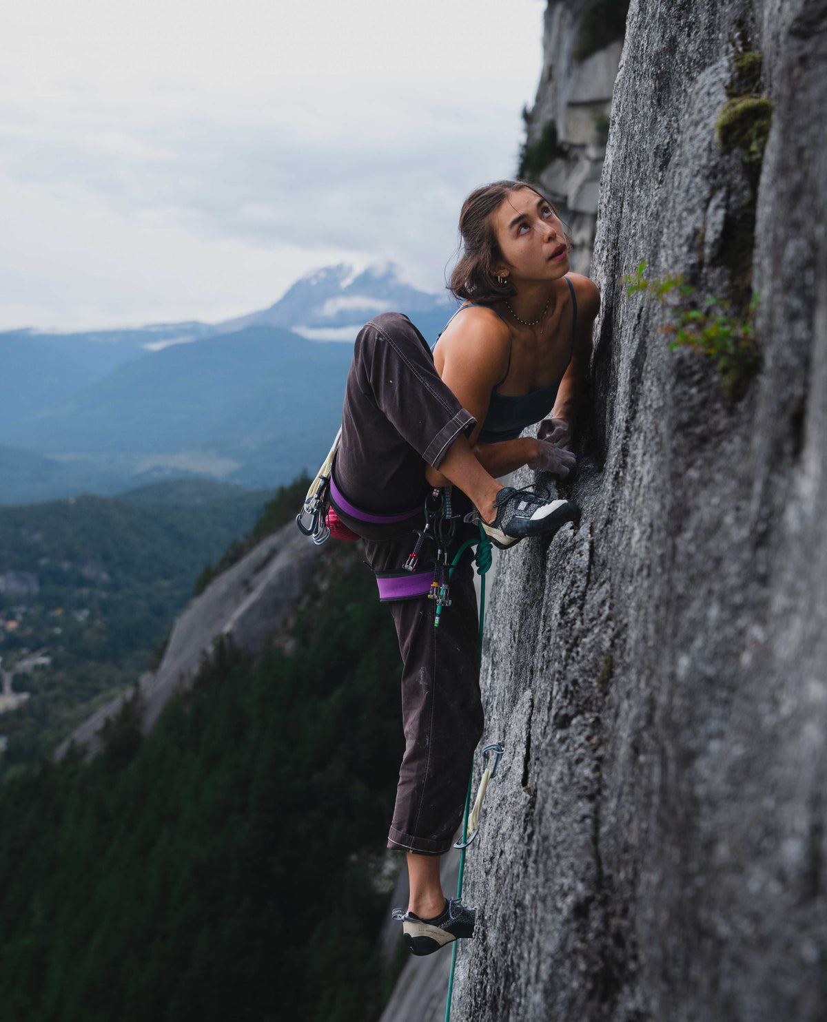 A woman climbing a rock wall wearing brown reggie pants