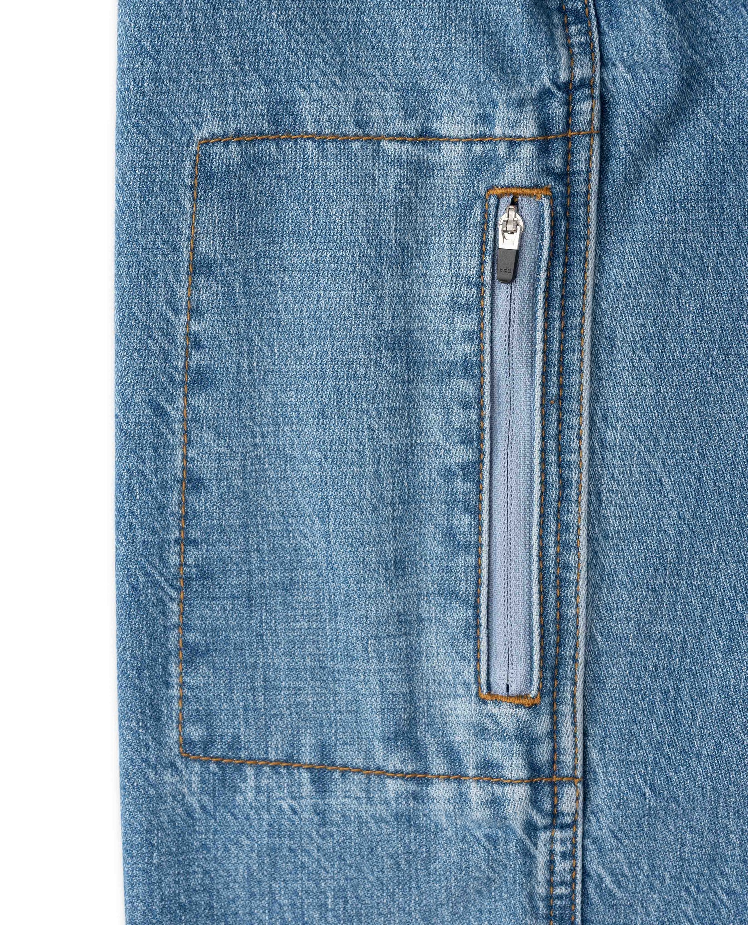 Close-up of a light blue denim jacket or pants leg showing a vertical zippered pocket with orange contrast stitching.