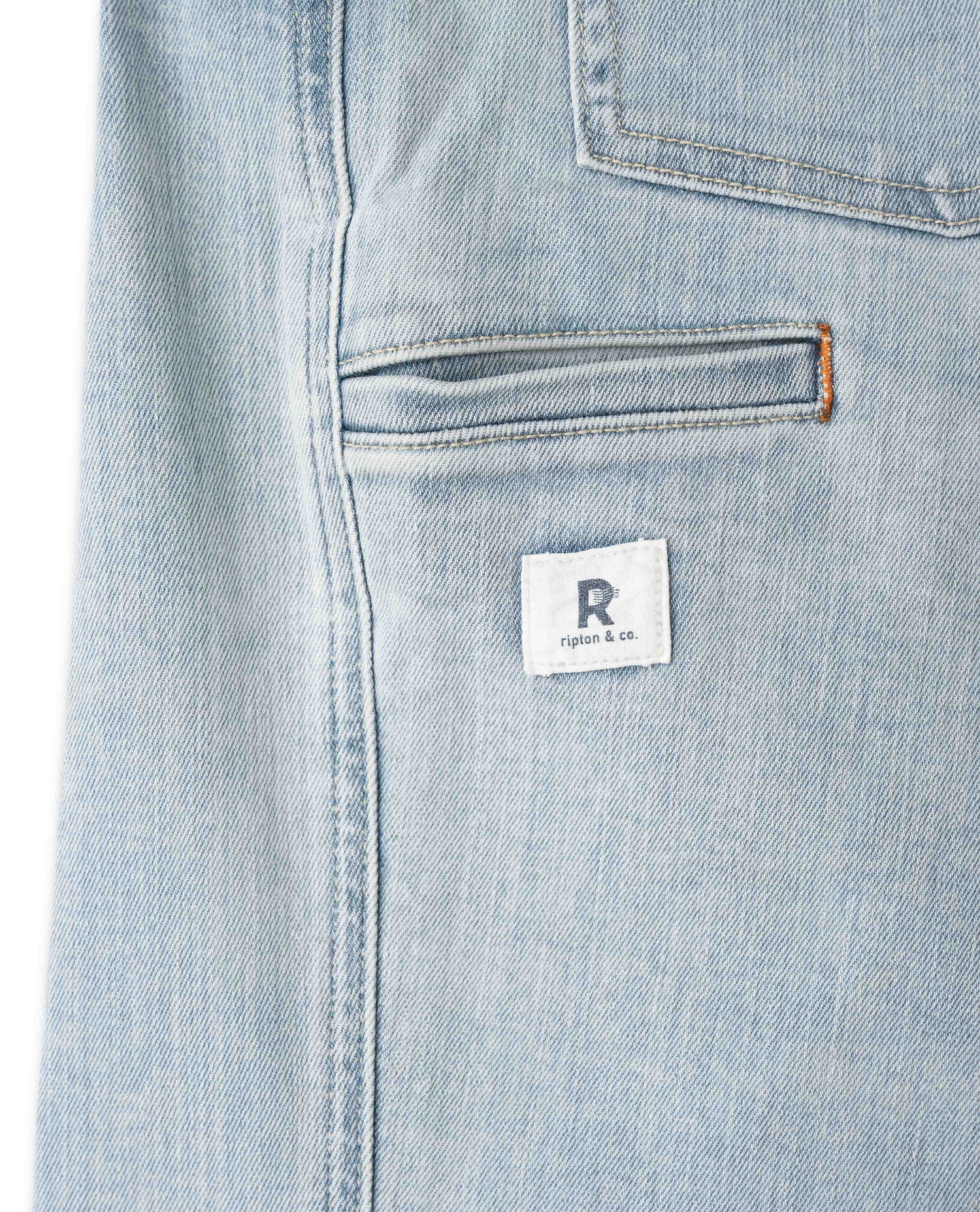 Close-up of light blue denim fabric with a brand label on a white background