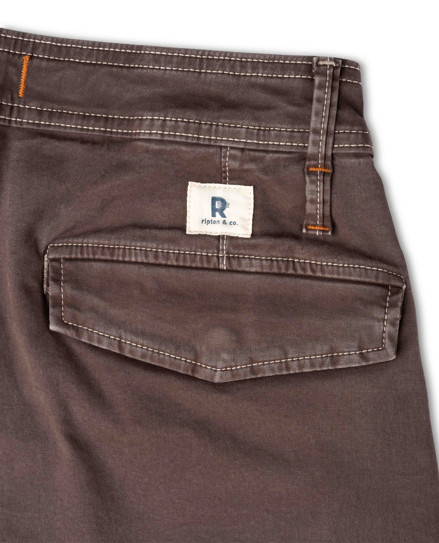Close-up of the back waistband and pocket of dark brown denim jeans, showing a white brand label that reads 'R Ripton & co.' with orange contrast stitching.