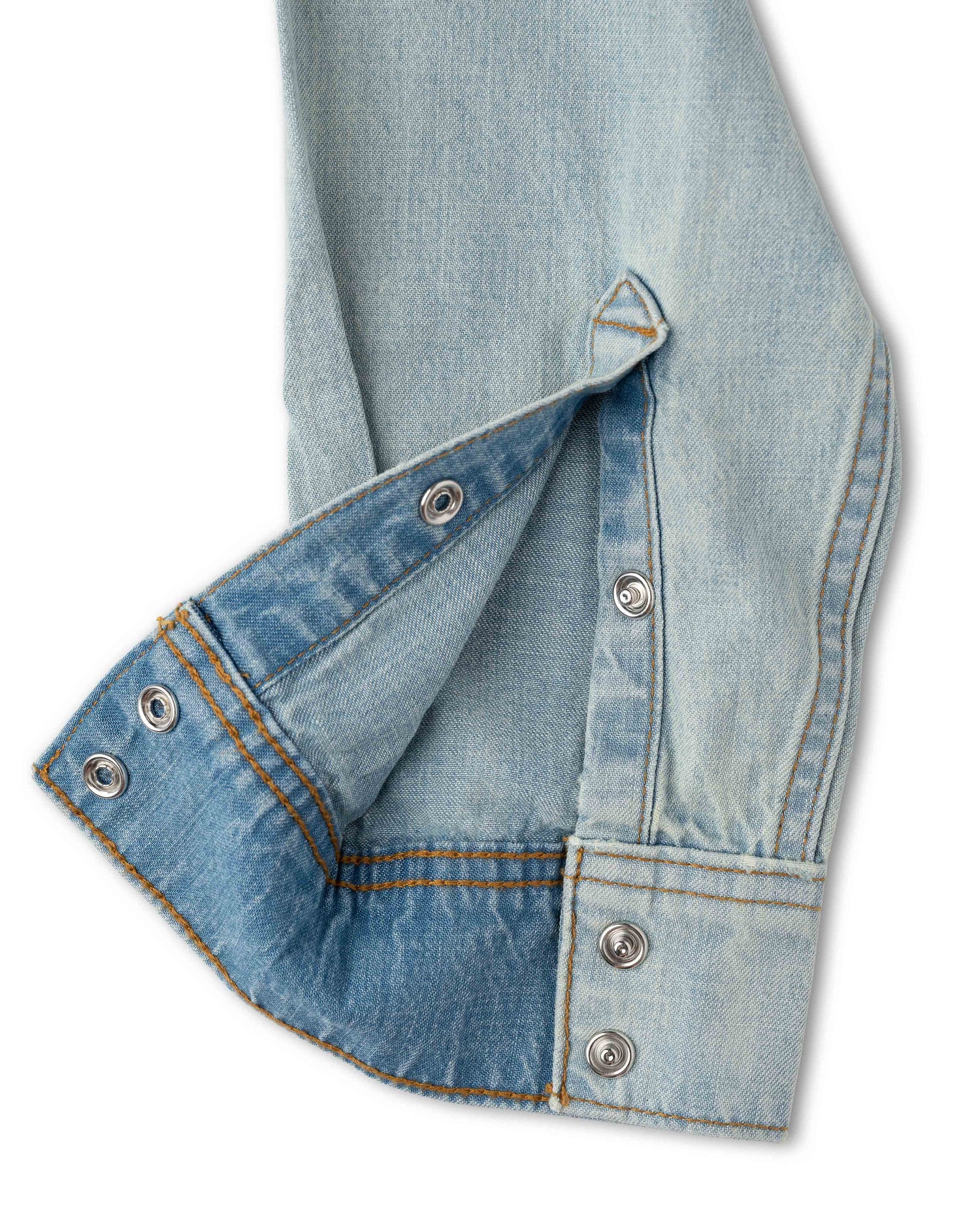 Close-up of a light blue denim shirt sleeve with a buttoned cuff and silver snap buttons, shown on a white background.