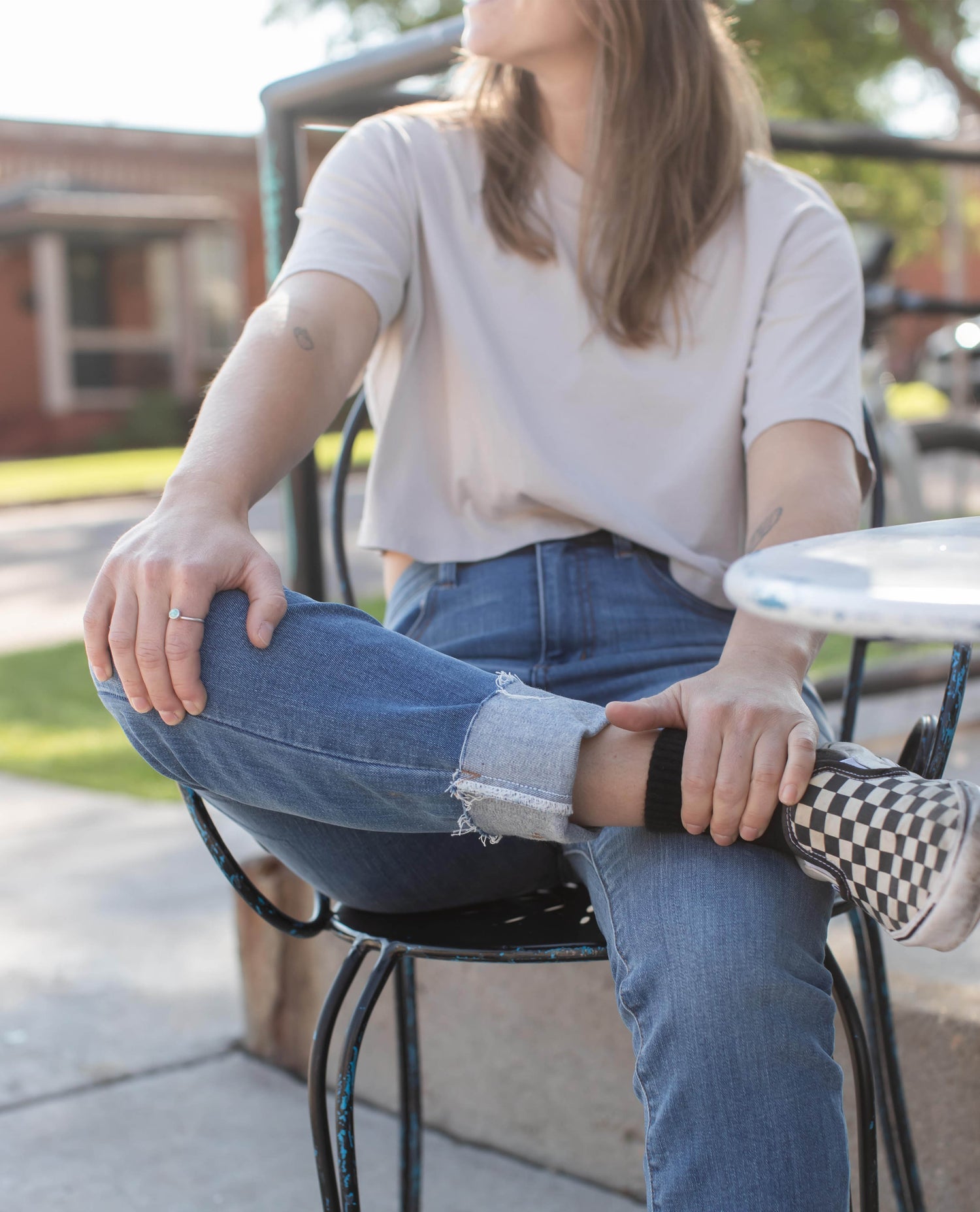 A close up of a pair of cuffed jeans. Model is sitting in a chair outside. 