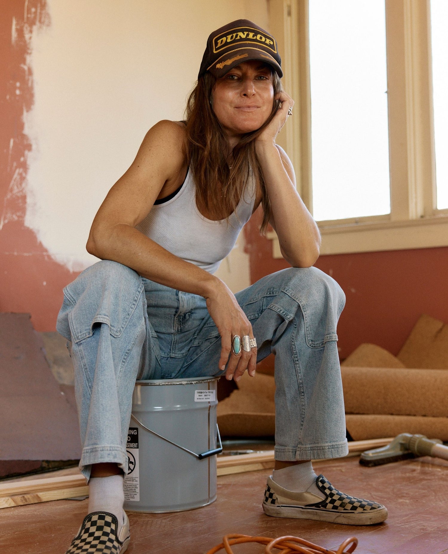 Person sitting on a bucket in a room under renovation wearing a Dunlop cap.