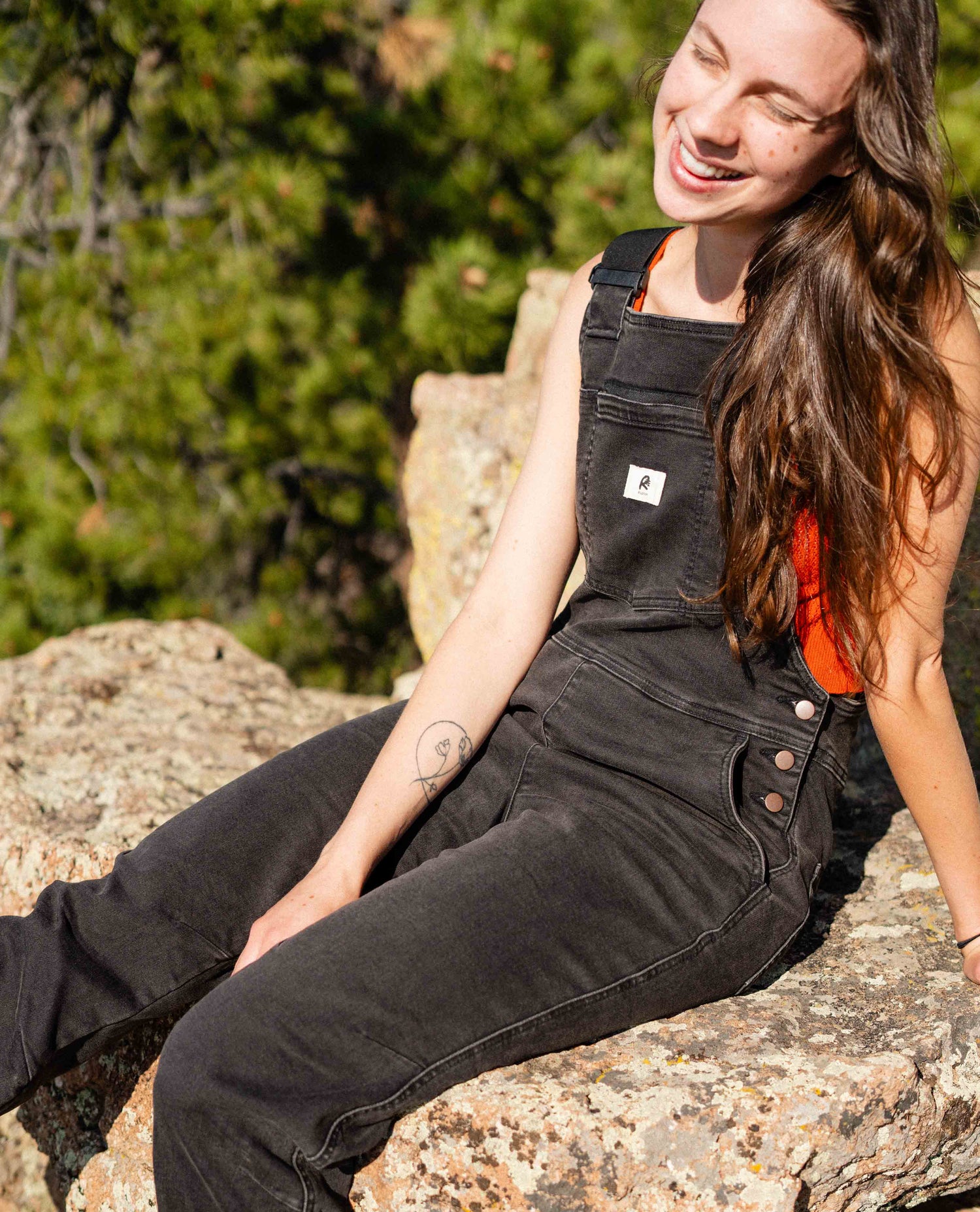 Girl sitting on rock in Ripton overalls. 