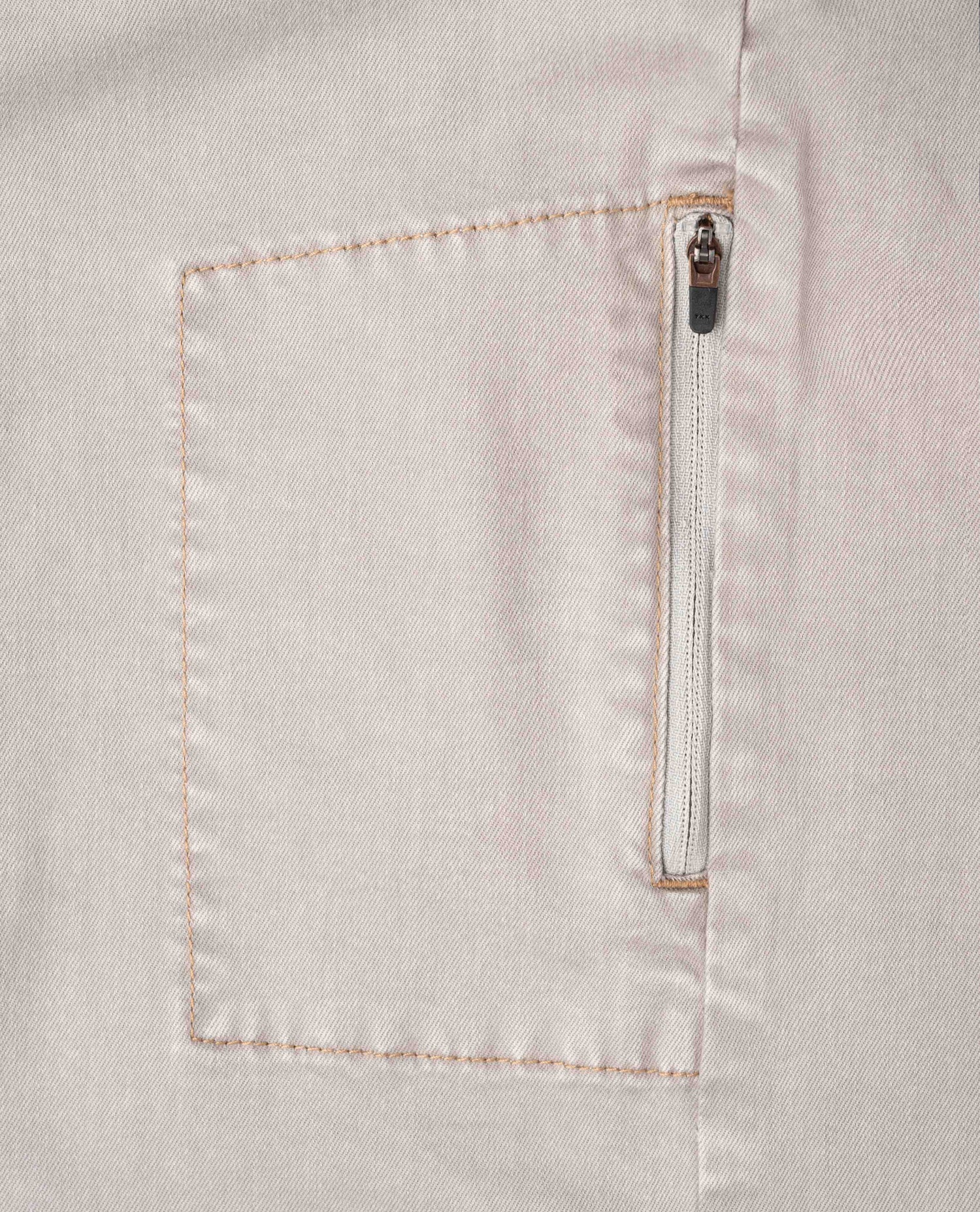 Close-up of a light-colored fabric pocket with a zipper on a matching background