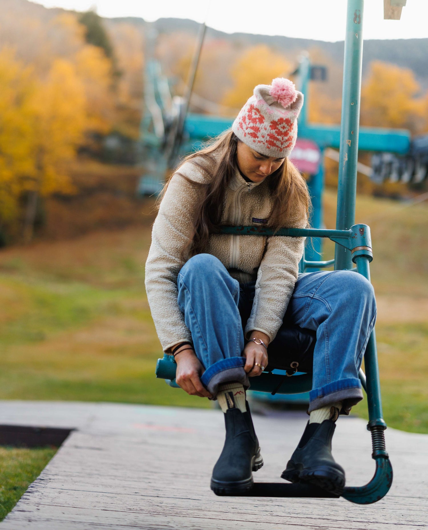 Person sitting on a green metal bench with autumn trees in the background