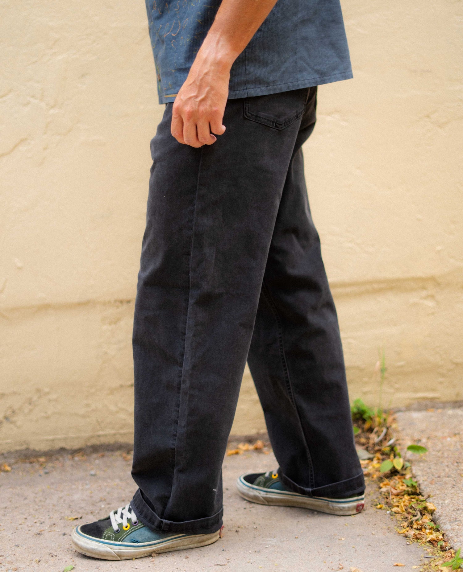 Person wearing black pants and blue shoes against a beige wall.