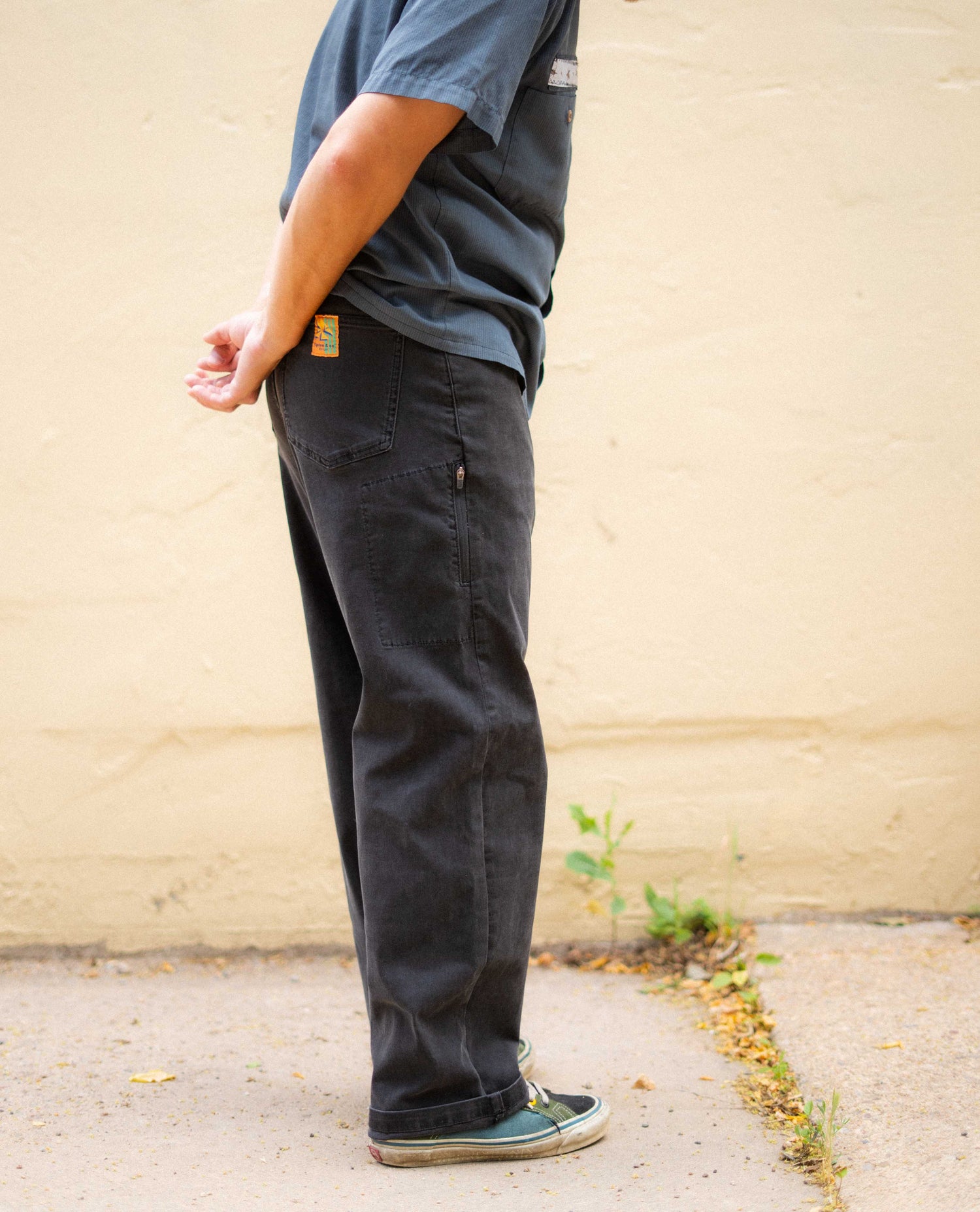 Person wearing dark pants and a blue shirt against a beige wall.