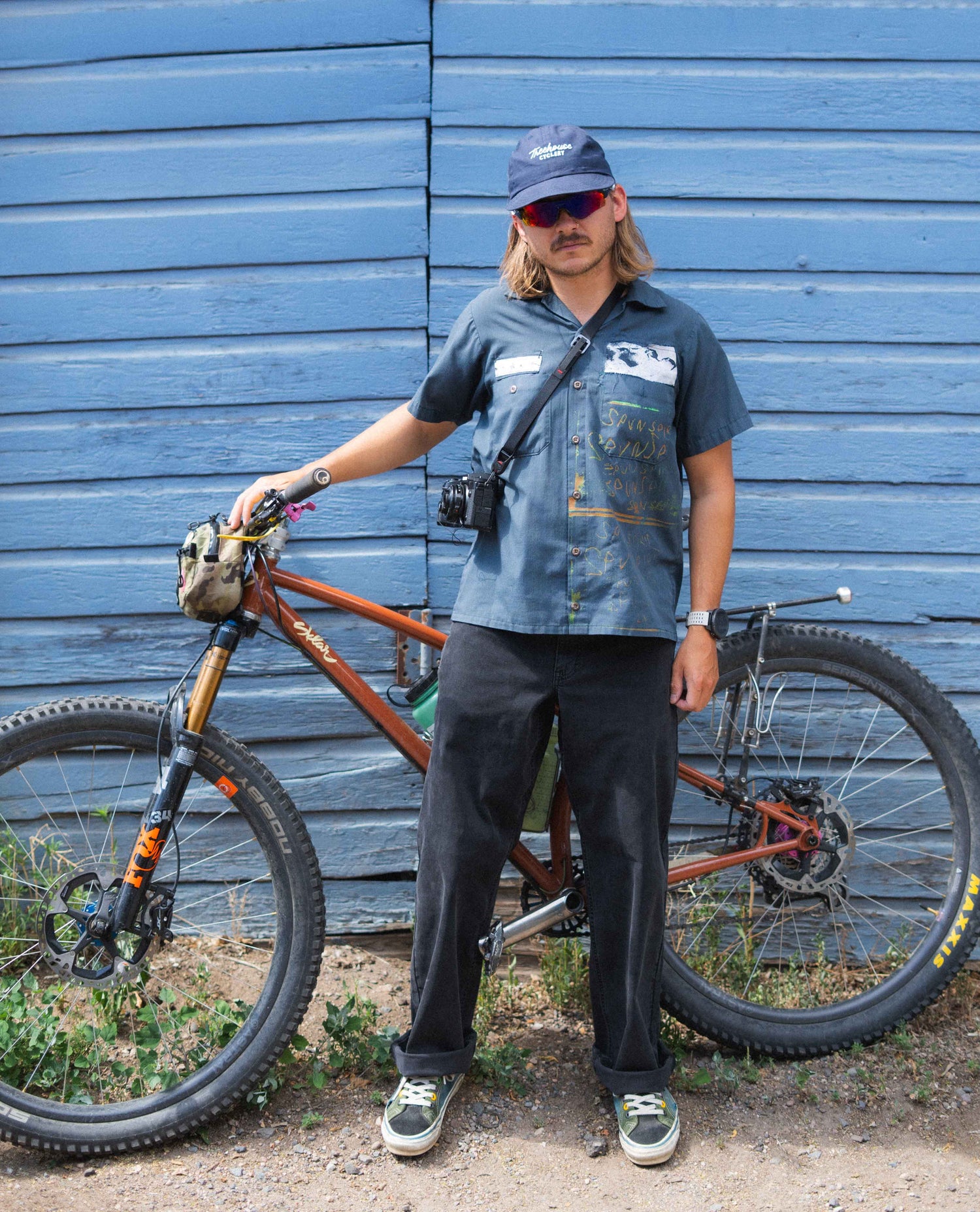 Person standing next to a bicycle against a blue wooden wall