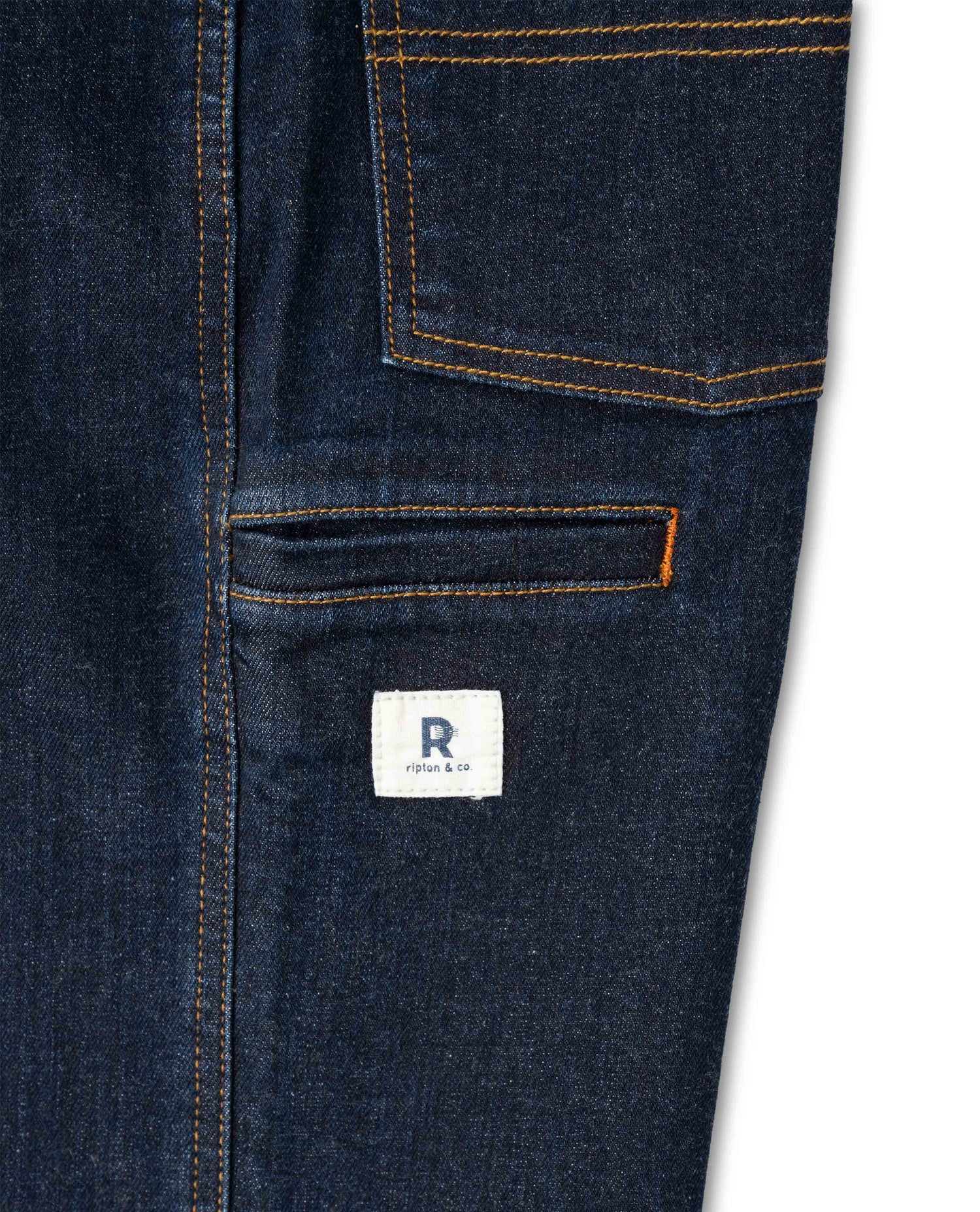 Close-up of dark blue denim pants with a brand logo on a white background