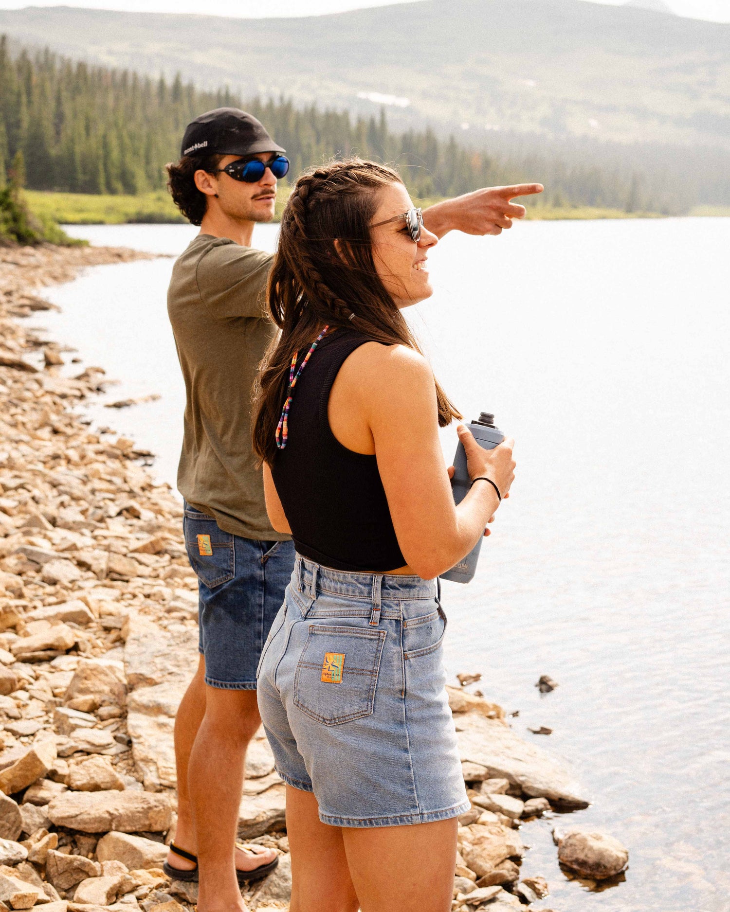 Woman standing in Ripton DTJ shorts near a mountain lake with a man pointing off screen behind her. 