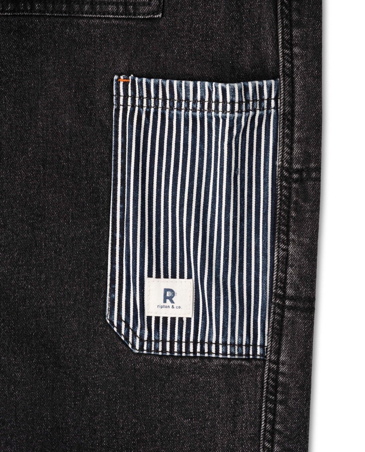 Close-up of a black denim jacket with a striped pocket and a brand logo.
