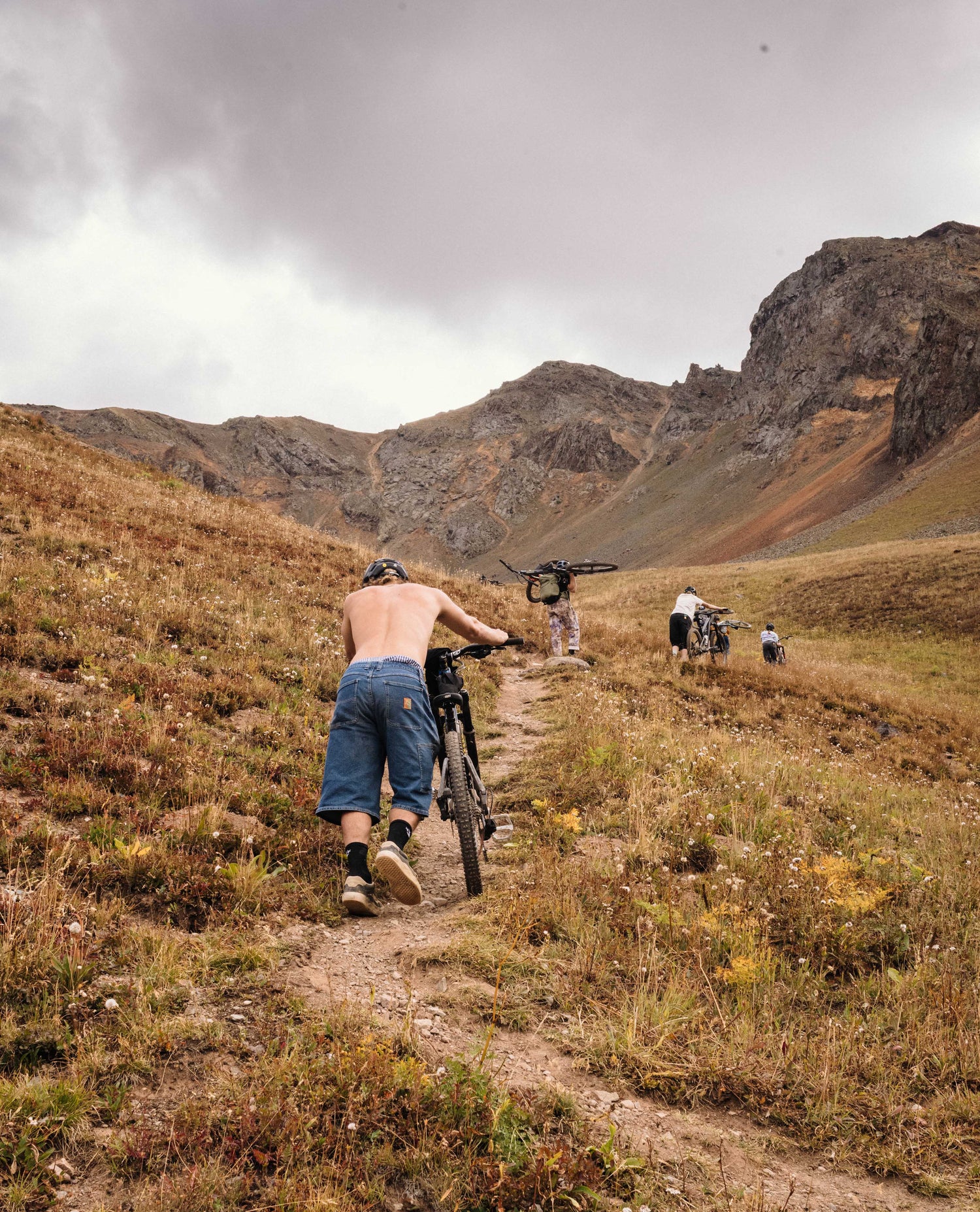 Man riding a bike on a mountain trail with rocky cliffs and overcast sky.