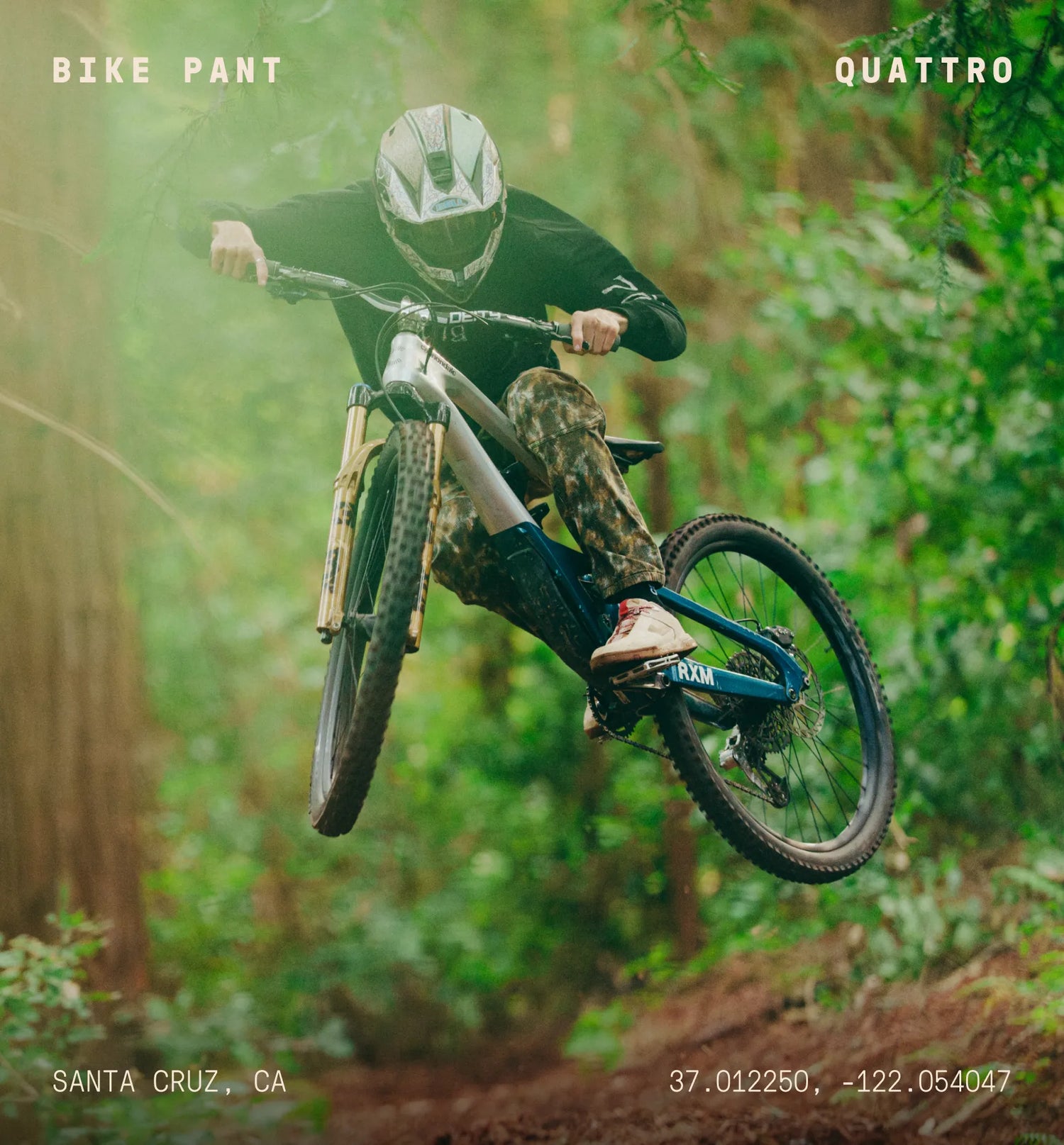 Person riding a mountain bike in a forest with 'BIKE PANT' and 'QUATTRO' branding.