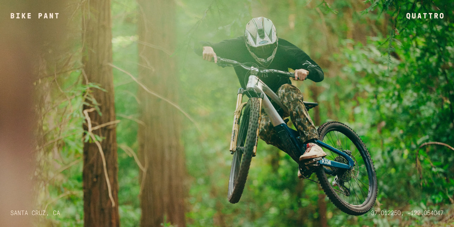 Person riding a mountain bike through a forest, with 'Bike Pant' and 'Quattro' branding visible.