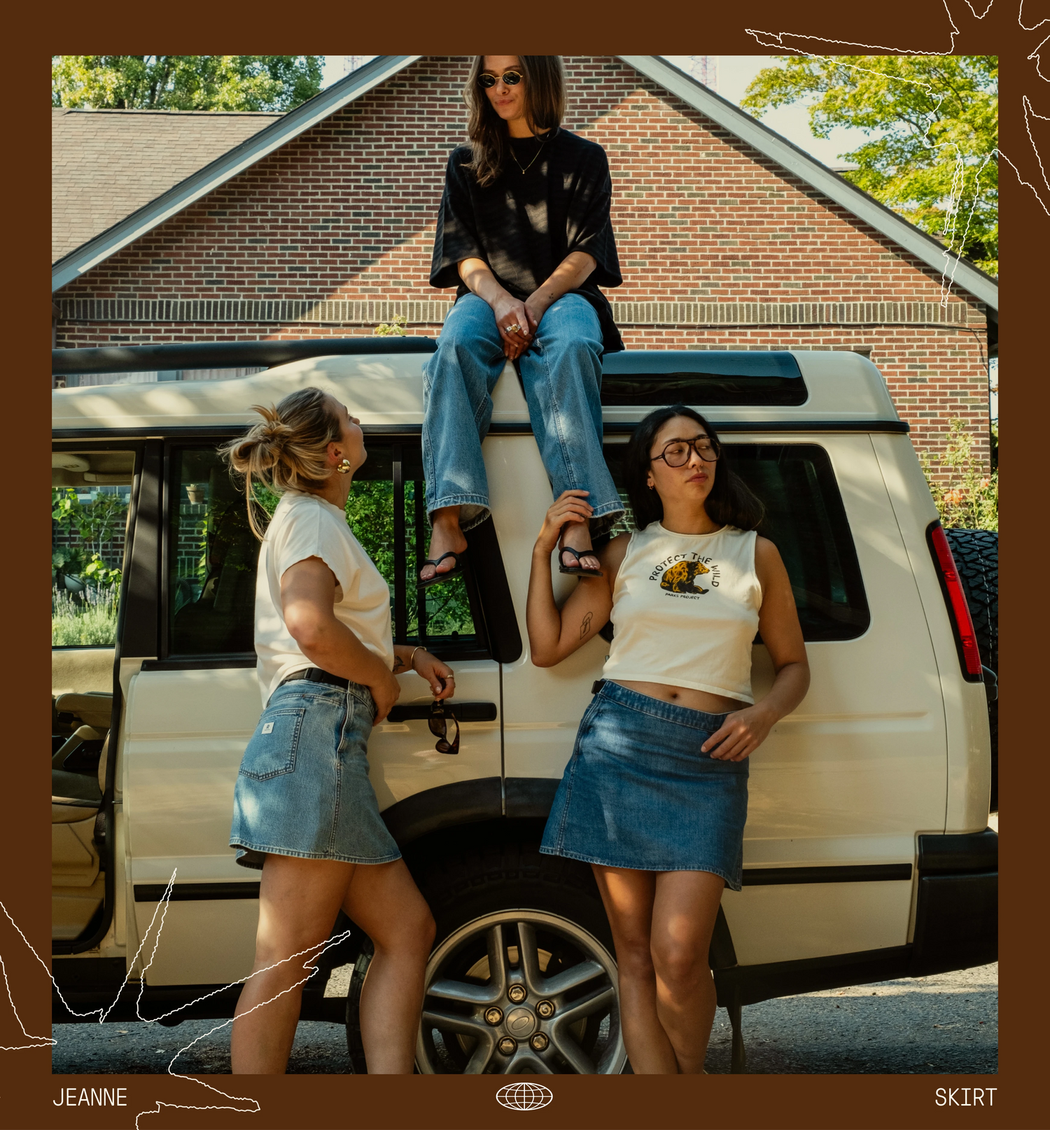 Three women pose in front of a cream-colored SUV in a backyard setting. One woman sits on the roof of the vehicle, while the other two stand on the ground, wearing matching white crop tank tops and denim skirts.