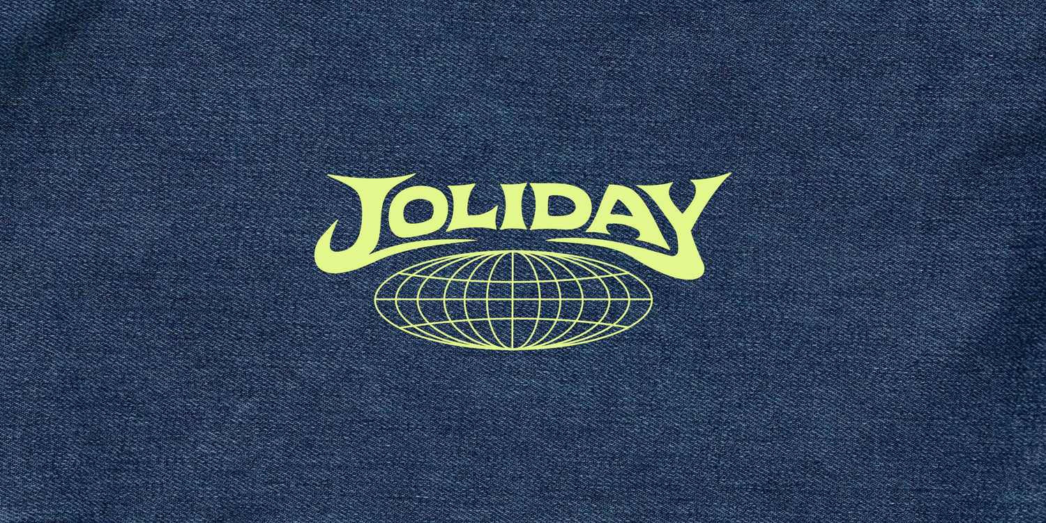 A close-up of a dark blue denim fabric featuring a lime green 'JOLIDAY' graphic logo with a globe design underneath.