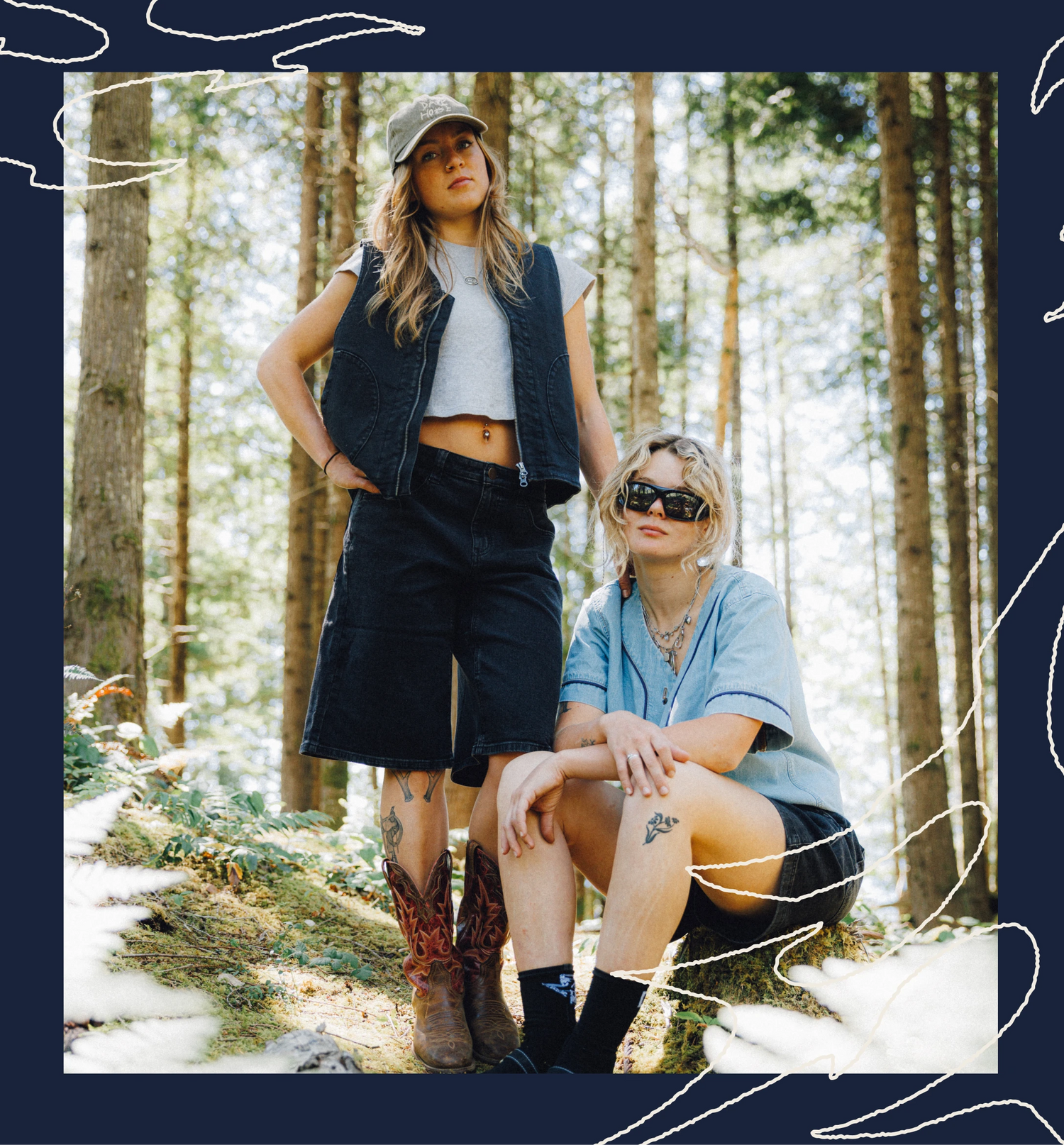 Two women posing in a sunlit forest. One stands wearing a black denim vest over a white crop top, black shorts, and brown cowboy boots.