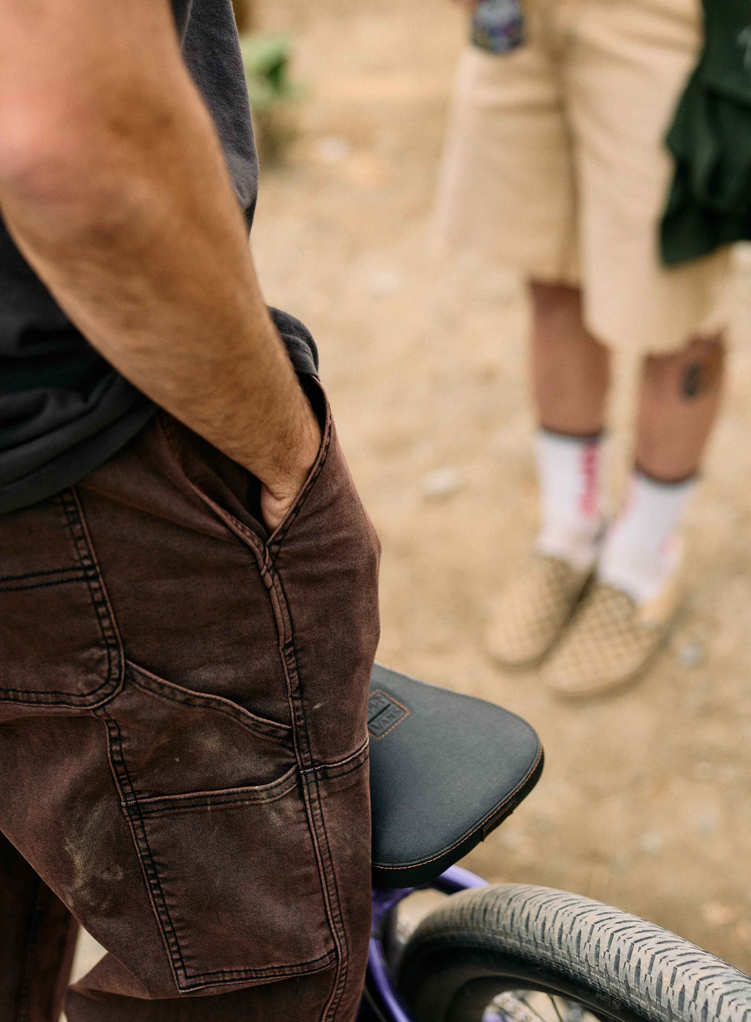 Person wearing brown pants sitting on a bike with another person in the background.