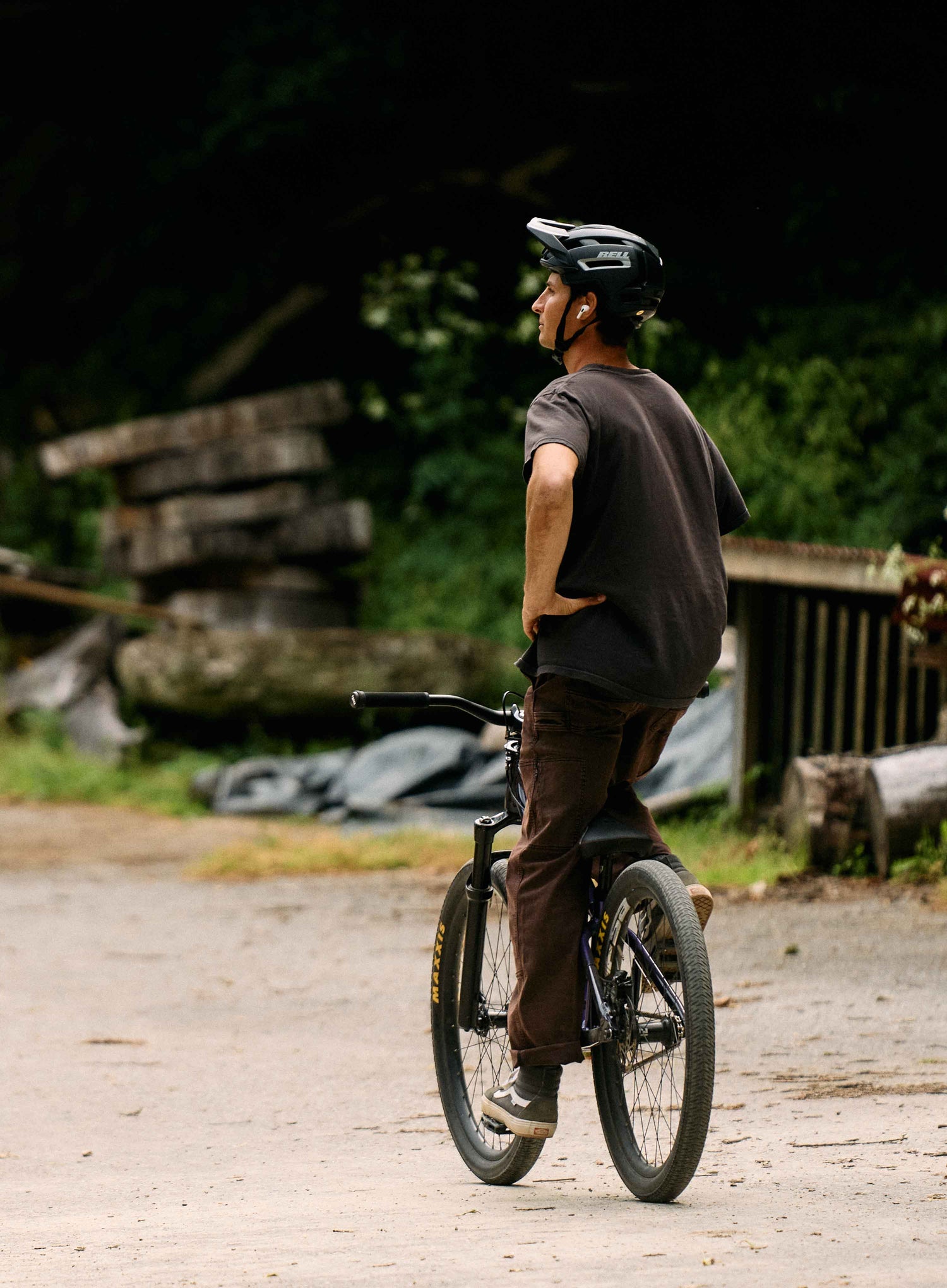 Person riding a bicycle on a dirt path with logs and greenery in the background