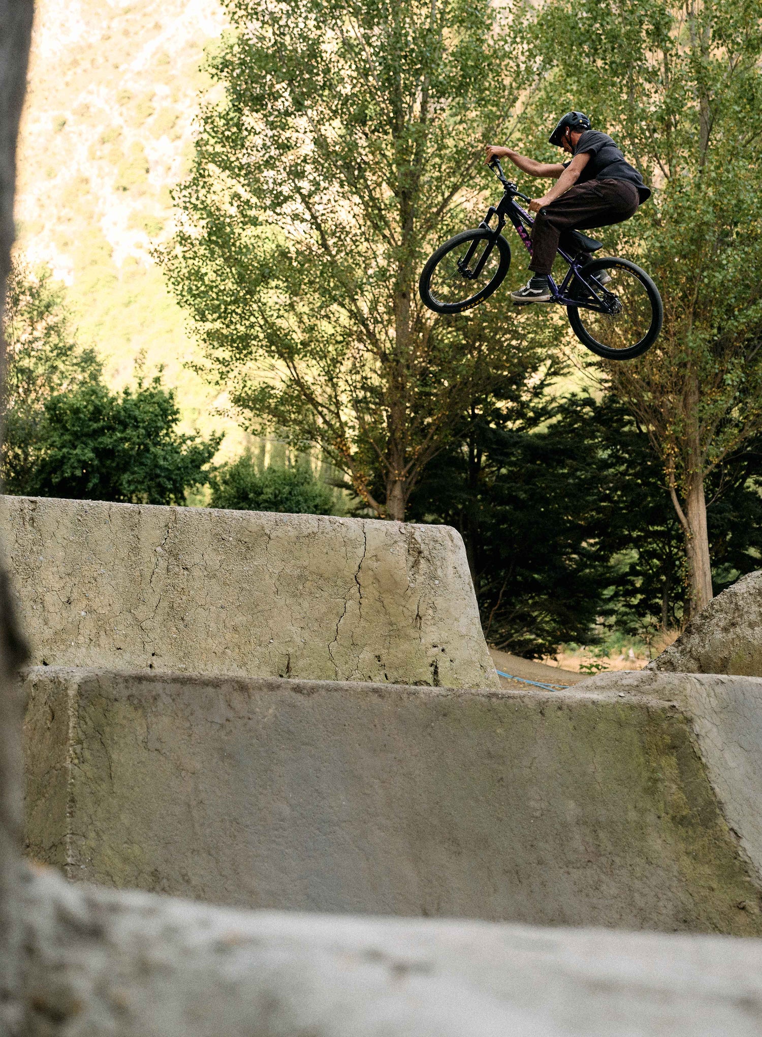 Person on a bicycle performing a jump over a concrete structure with trees in the background