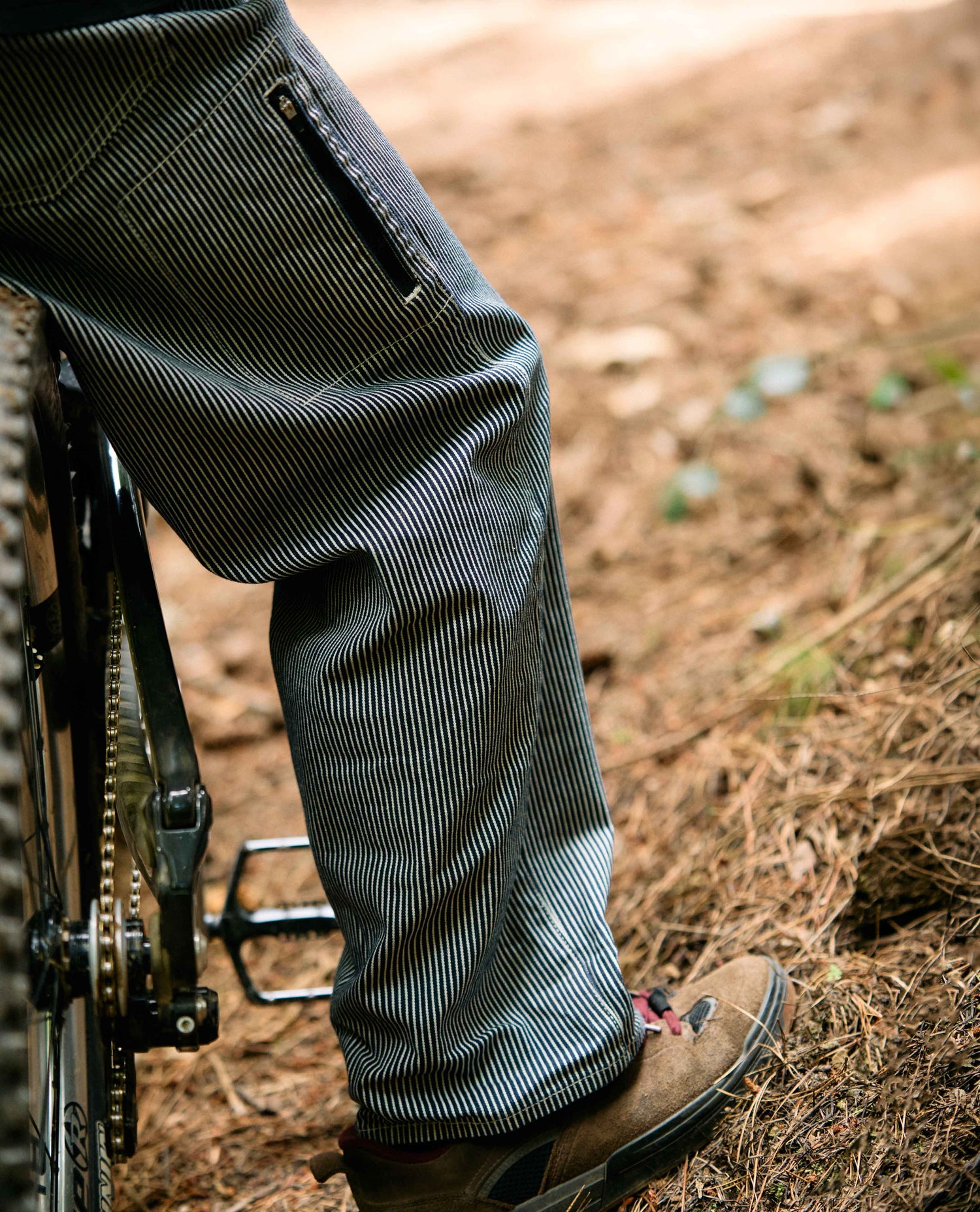 Person wearing dark pants and brown shoes on a dirt path