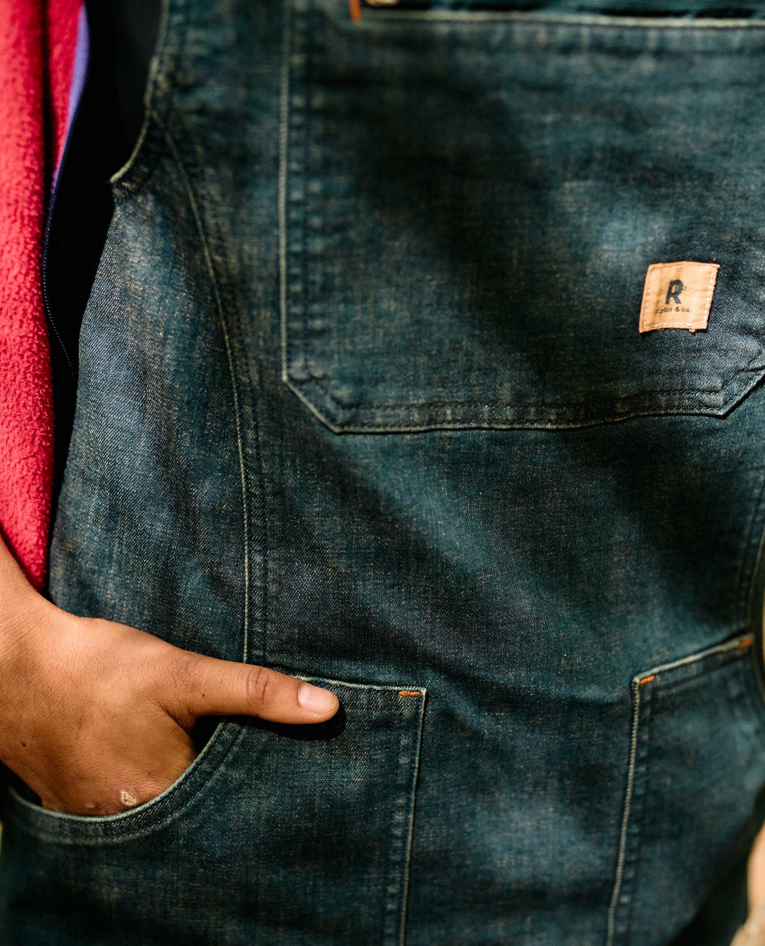 Close-up of dark blue jeans with a brand logo on the pocket, worn by a person.