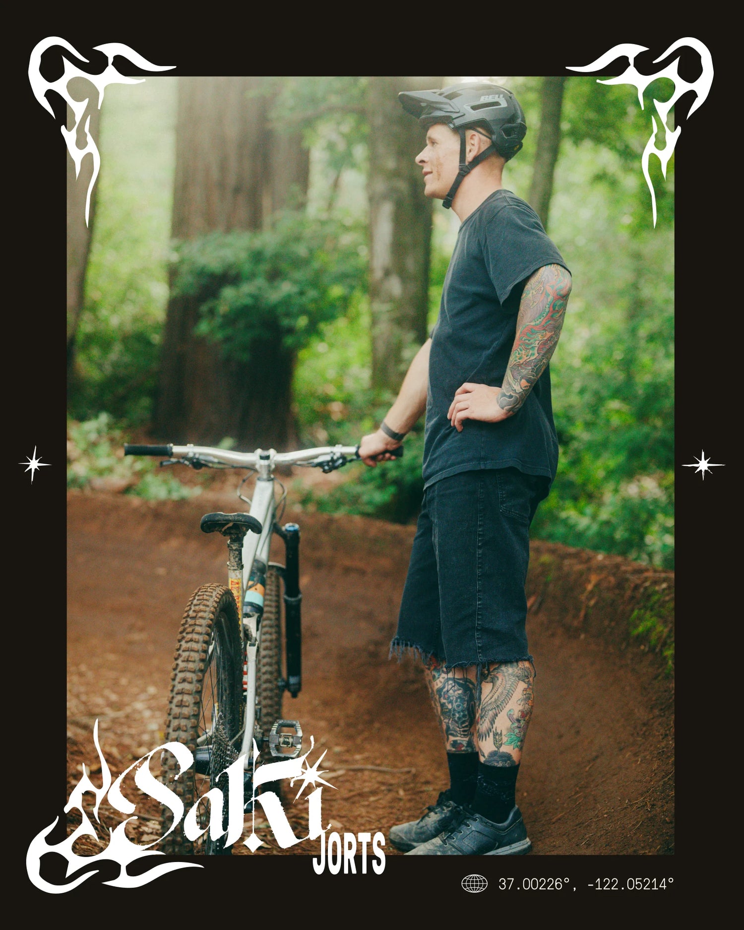 Person with tattoos holding a mountain bike in a forest, wearing Saki Jorts.