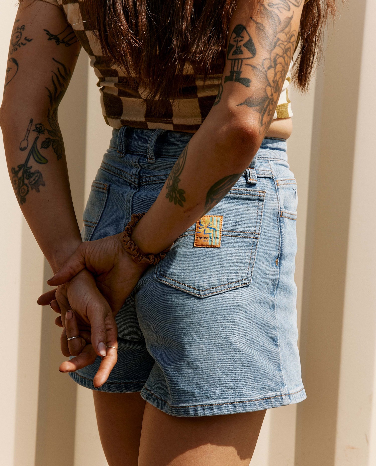 Woman standing in front of a shipping crate wearing a checkered crop top and jean shorts with white shoes. 